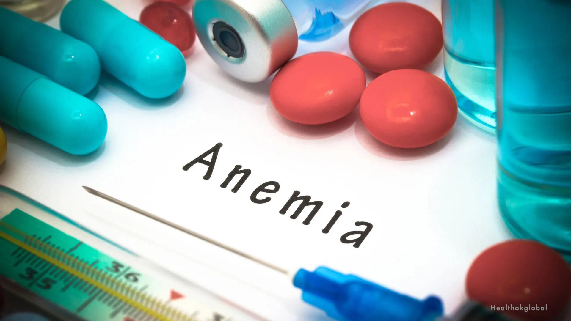 Anemia treatment concept with iron supplements, vitamin capsules, thermometer, syringe, and the word 'Anemia' written on paper.