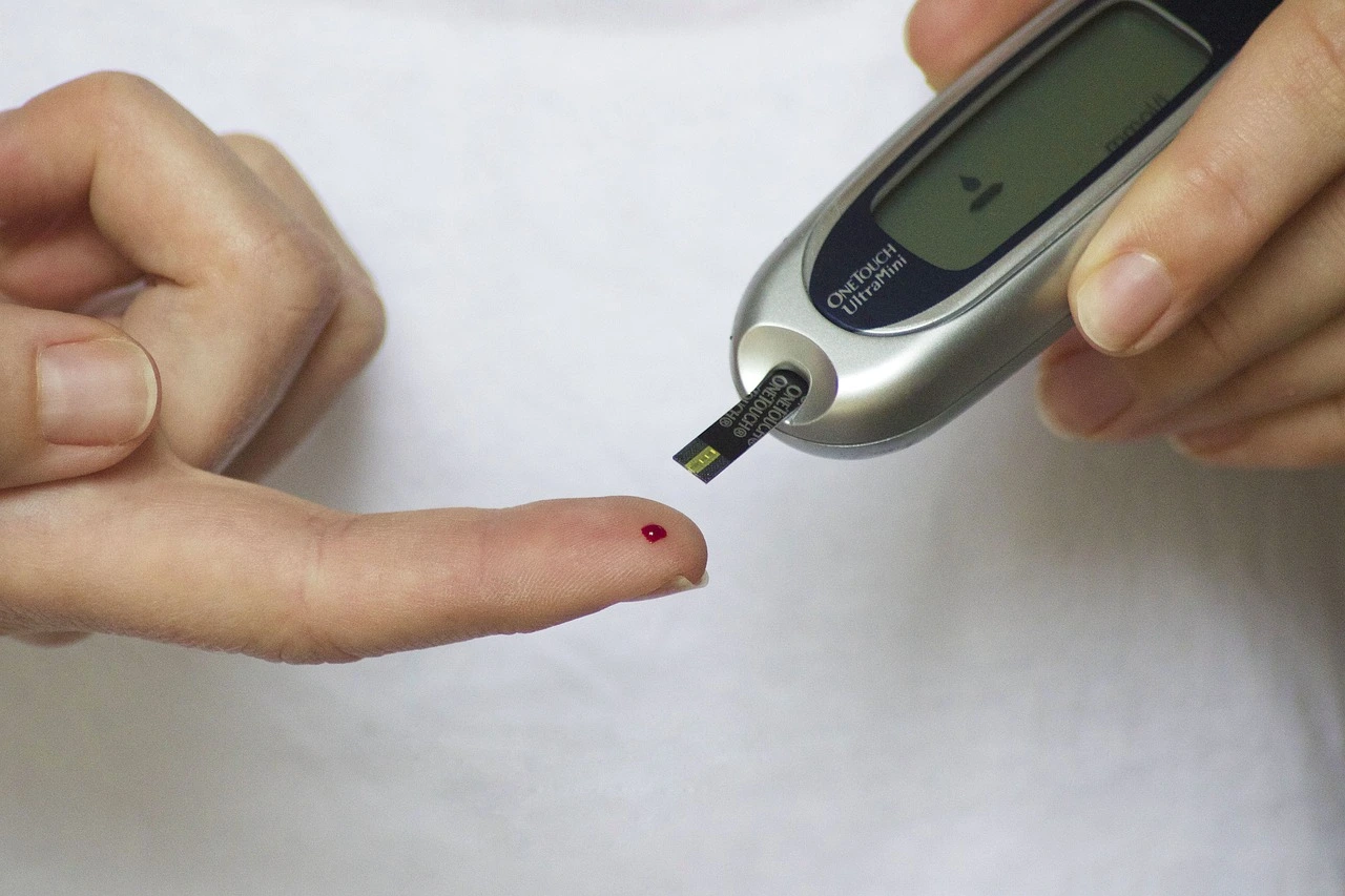 Close-up of a person's hand performing a blood sugar test using a glucometer. A small blood drop is visible on the fingertip, emphasizing diabetes monitoring and glucose management.