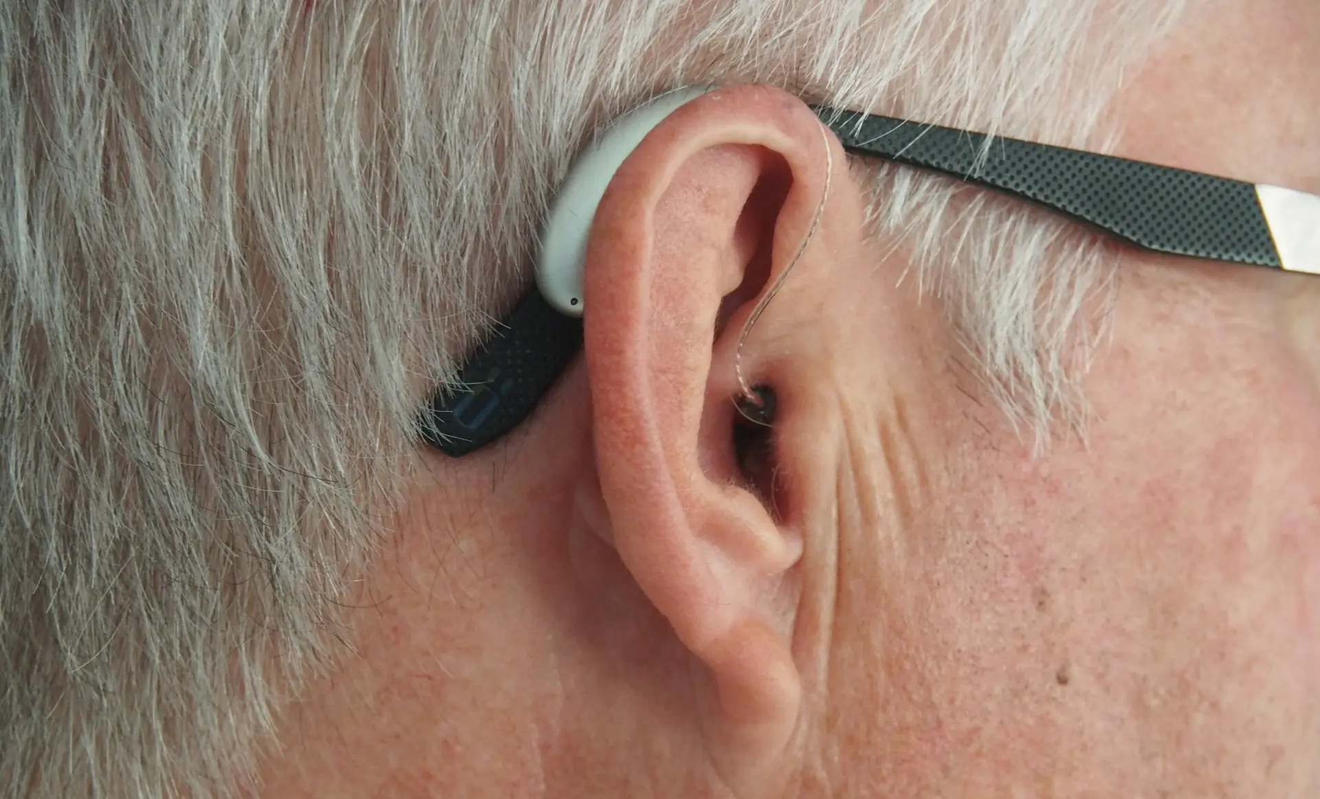 Close-up of an elderly person wearing a hearing aid to improve hearing ability, showcasing modern hearing assistance devices for managing hearing loss.