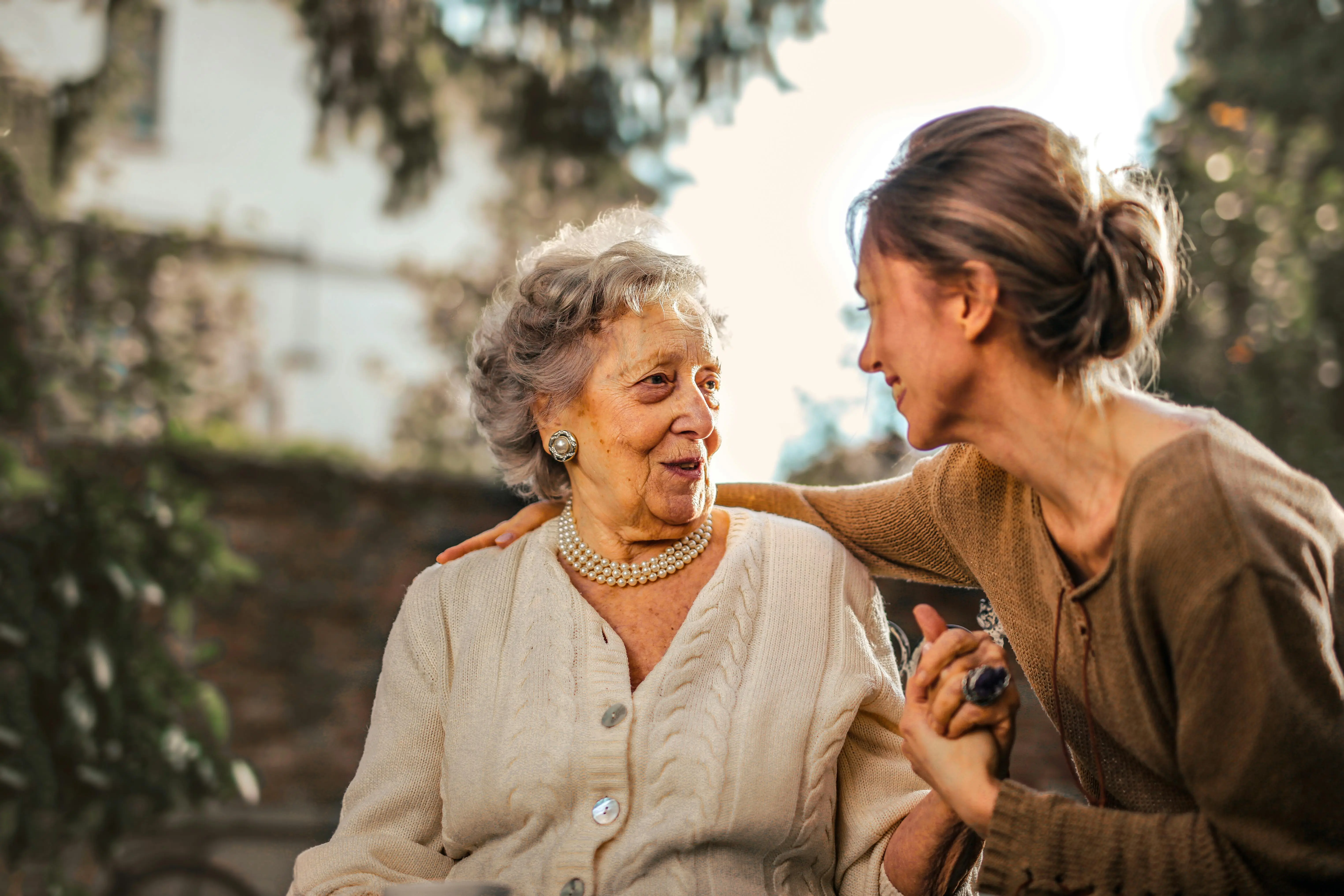 Elderly woman smiling while receiving care and support from a female caretaker in an outdoor setting, symbolizing professional caretaker services and companionship for seniors.