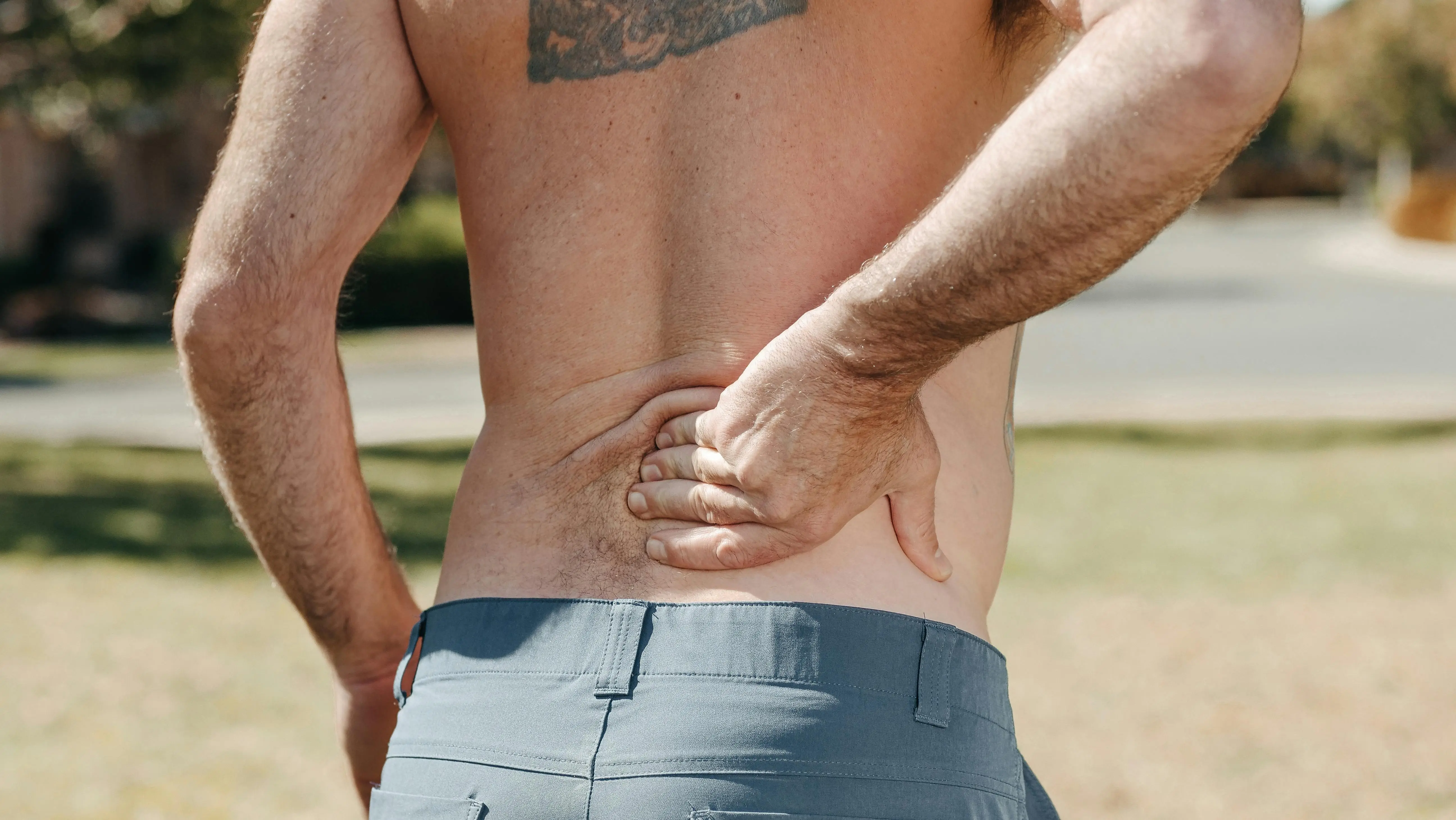 Man holding his lower back outdoors, experiencing discomfort, illustrating the need for effective tips on managing and relieving lower back pain.