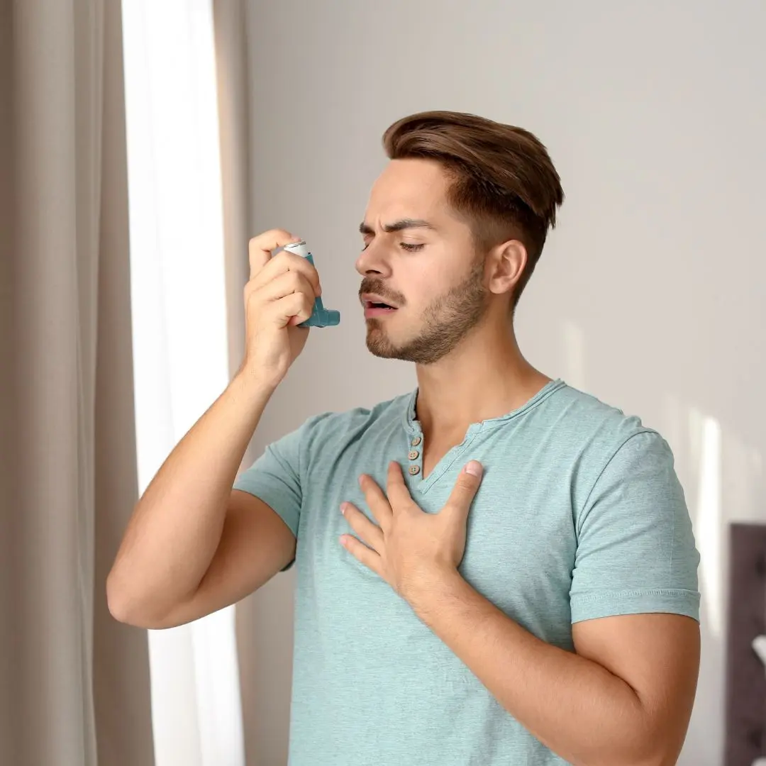 Young man experiencing asthma symptoms using an inhaler for respiratory relief, highlighting asthma management and treatment for airway inflammation.