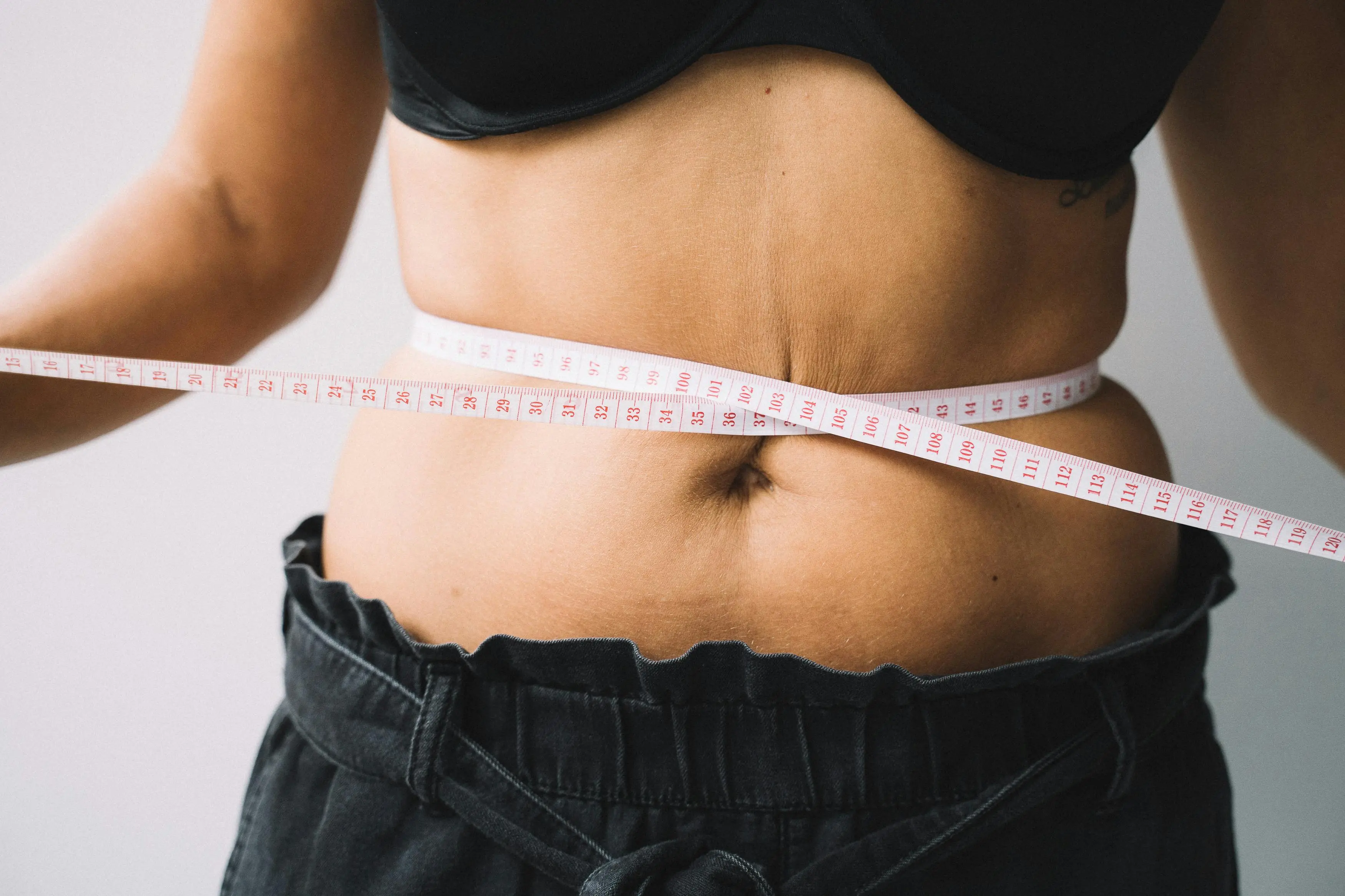 Close-up of a person measuring their waist with a tape measure, symbolizing healthy weight loss progress and body measurement tracking for fitness goals.