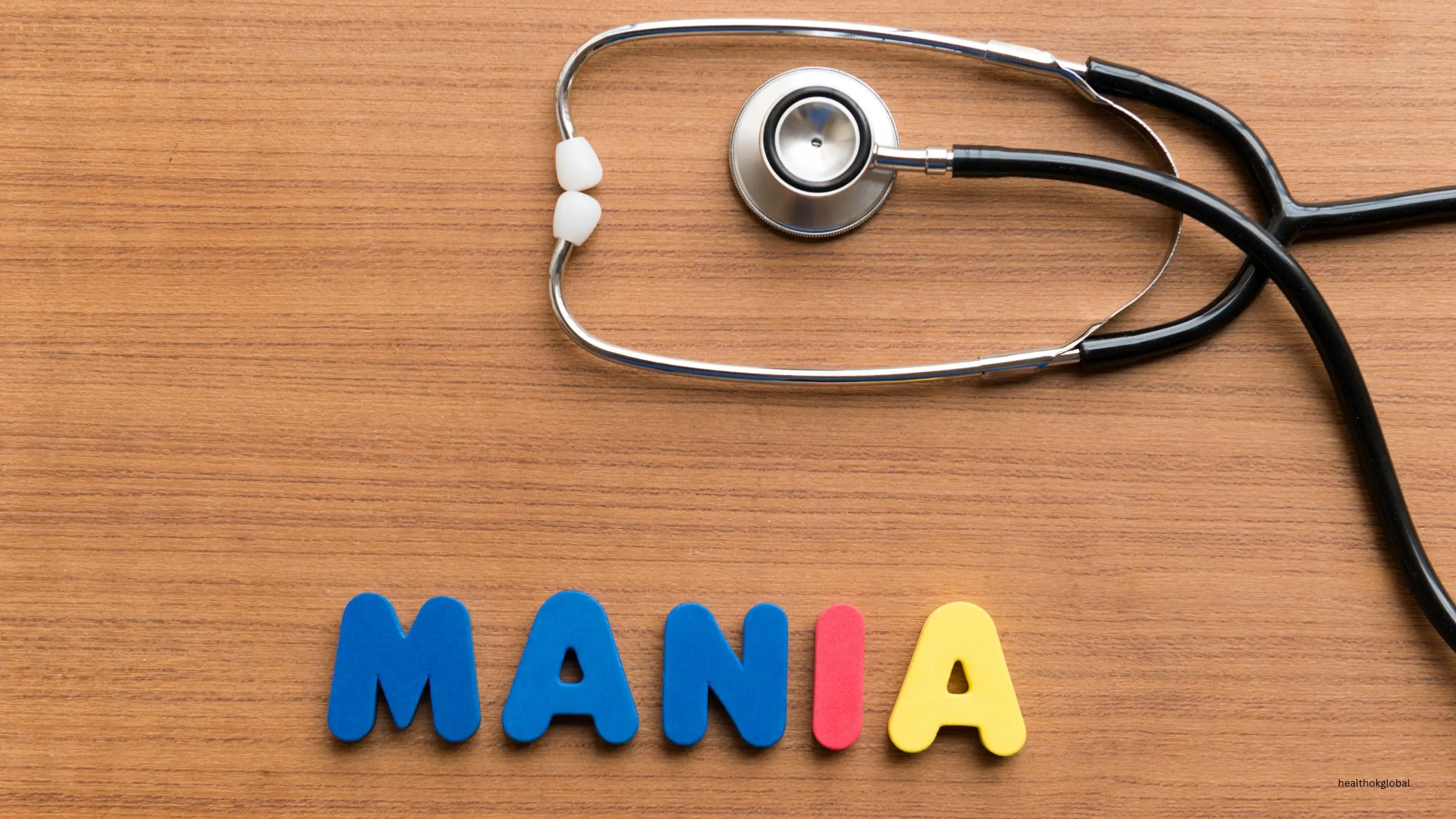 Nursing care plan for mania featuring a stethoscope and colorful word 'mania' on a wooden table, symbolizing healthcare strategies for managing mental health conditions.