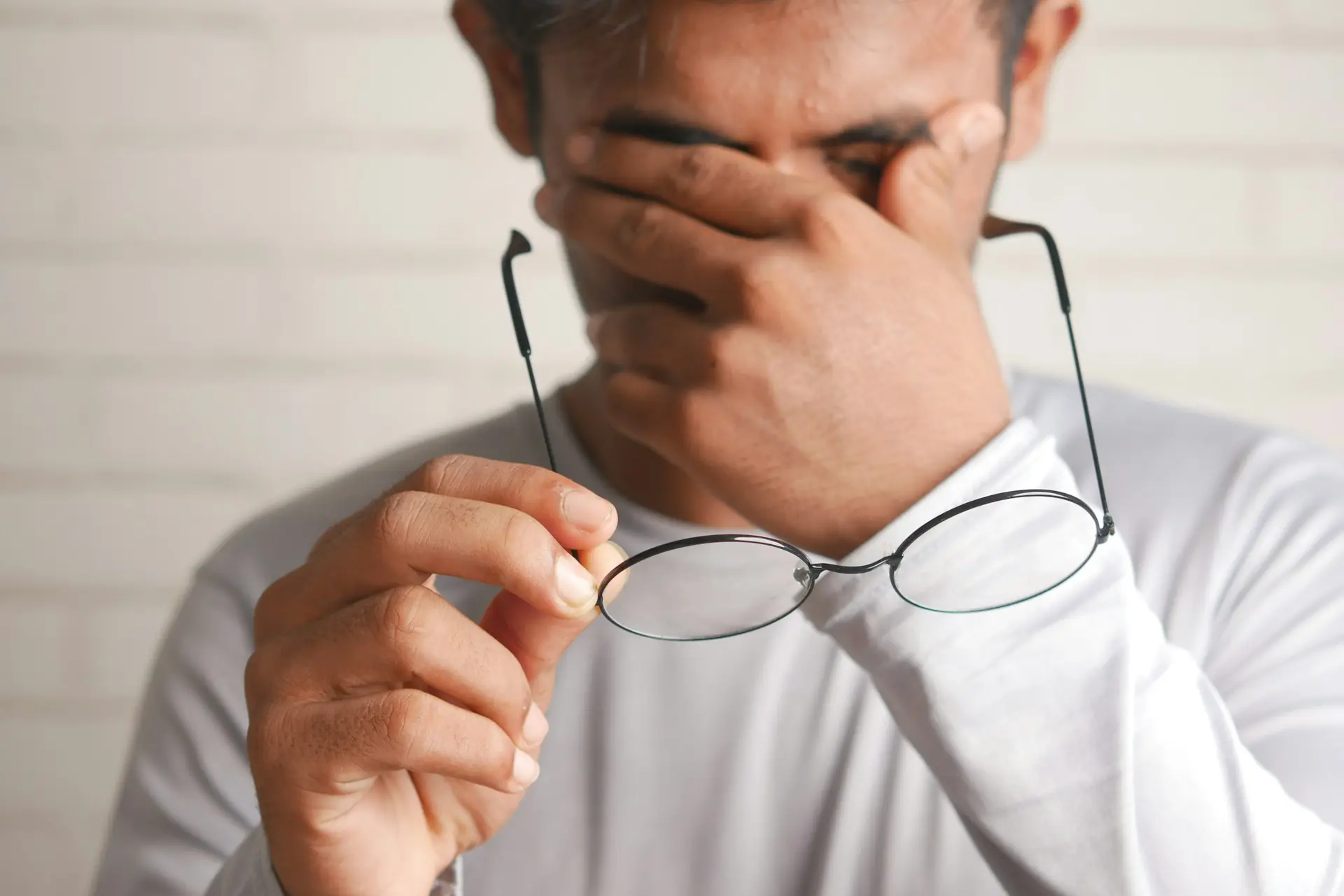 Man experiencing fatigue after eating, holding glasses in hand, highlighting symptoms potentially linked to postprandial drowsiness or diabetes.