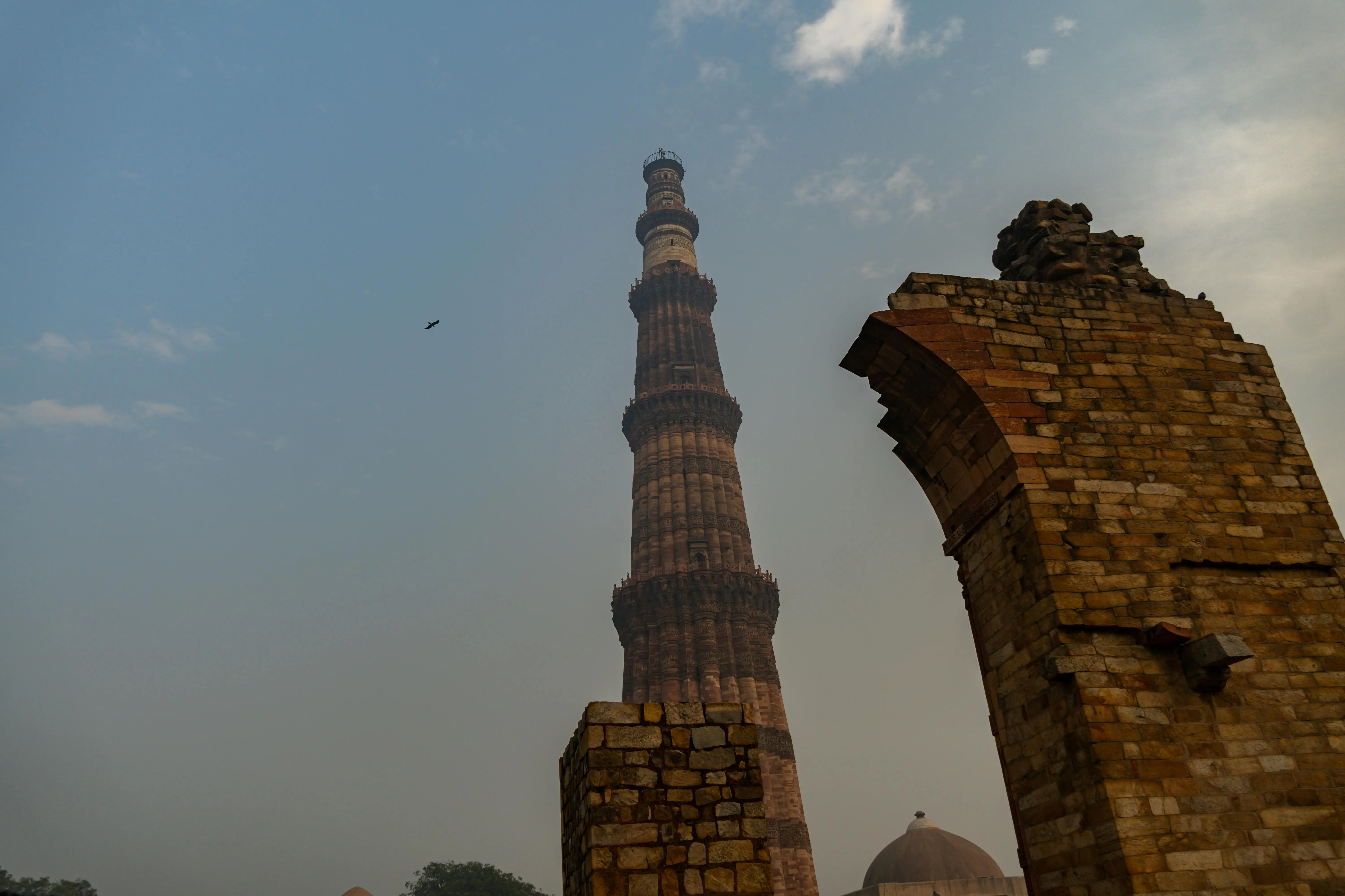 Historic Qutub Minar in Delhi with surrounding architectural ruins under a clear sky, showcasing ancient Mughal architecture and cultural heritage.