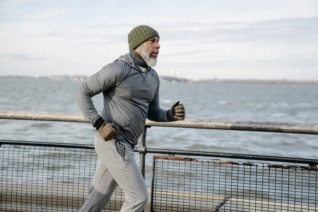 Senior man jogging along a waterfront, embracing a healthy lifestyle and staying active in cold weather for improved fitness and overall well-being.