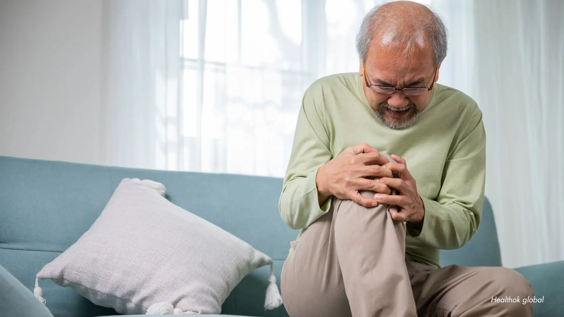 Senior man experiencing knee pain while sitting on a sofa, highlighting the importance of effective pain management solutions for elderly individuals.