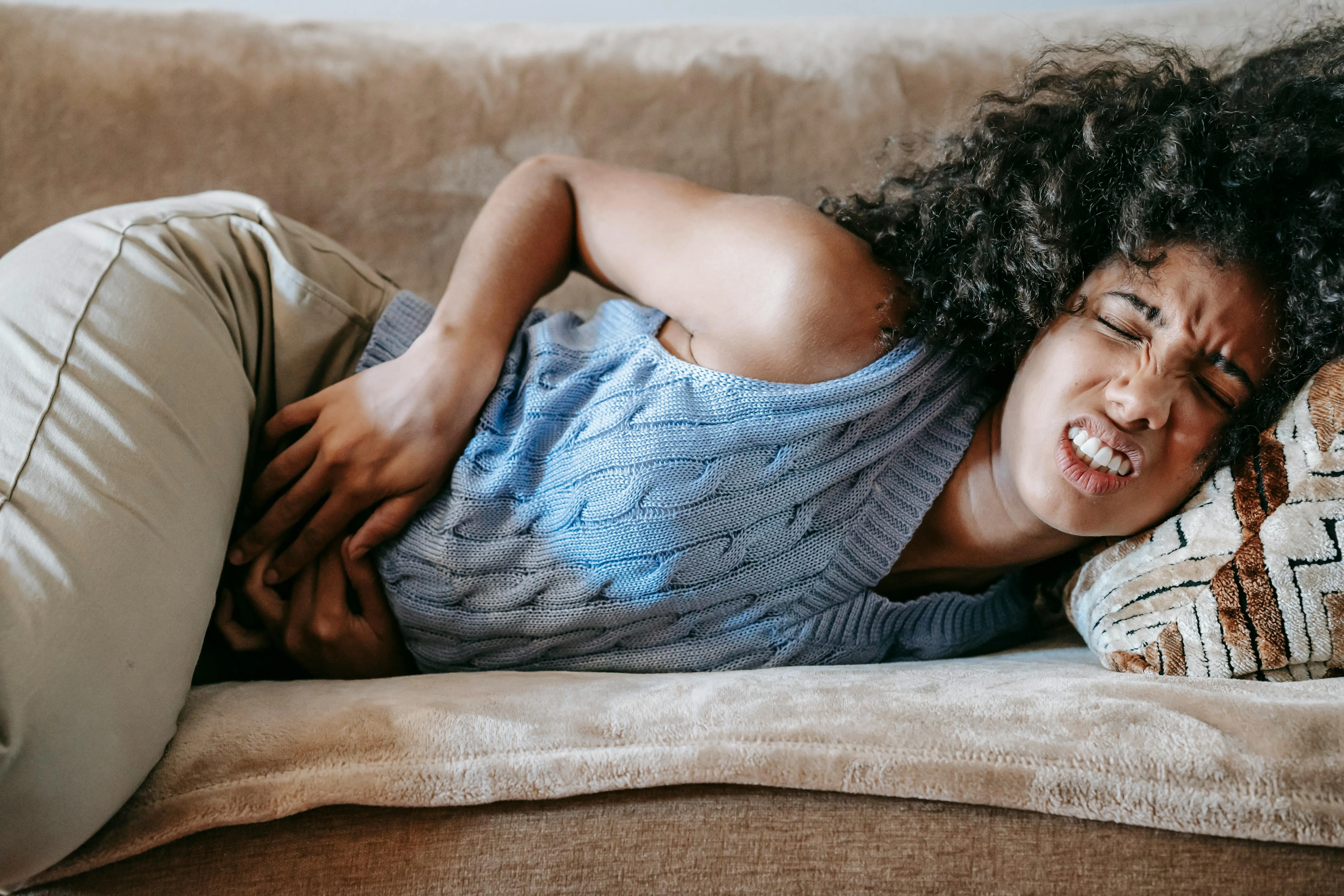 Woman experiencing abdominal discomfort and cramping due to constipation while lying on a couch.