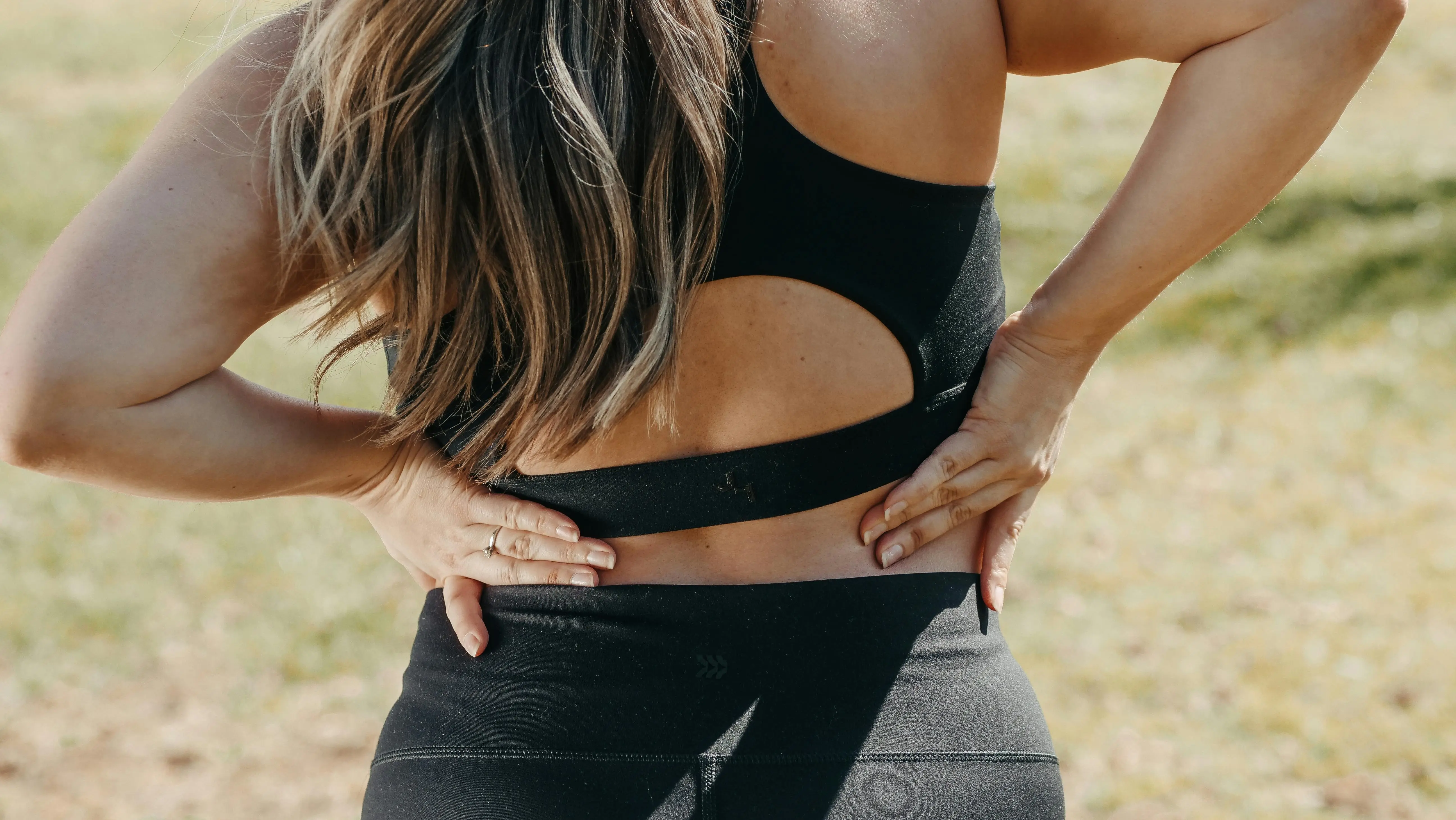 Close-up of a woman holding her lower back outdoors, symbolizing low back pain relief exercises for better mobility and reduced discomfort.